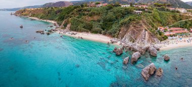Plajın ve şemsiyelerin havadan görünüşü. Tropea, Calabria, İtalya. Parghelia. Yukarıdan görünen deniz yatağının genel görünümü, şeffaf su. Yüzücüler, suda yüzen banyocular. Vardanello sahilleri ve kayalıkları