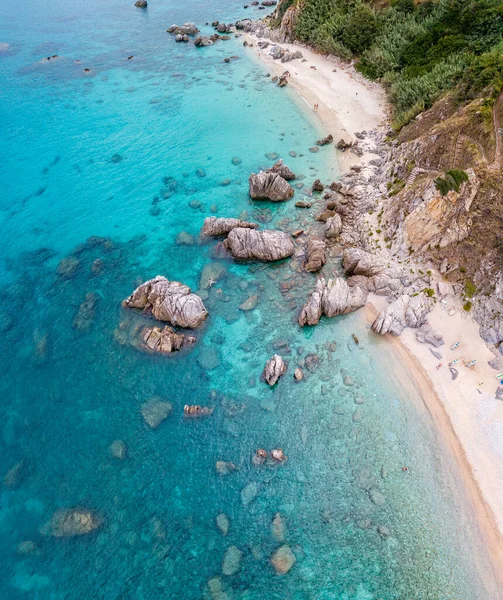 Aerial view of a beach and umbrellas. Tropea, Calabria, Italy. Parghelia. Overview of seabed seen from above, transparent water. Swimmers, bathers floating on the water. Beach and rocks of Vardanello — Stock Image Aerial View Beach Umbrellas Tropea Calabria Italy Parghelia Overview Seabed Stock Image