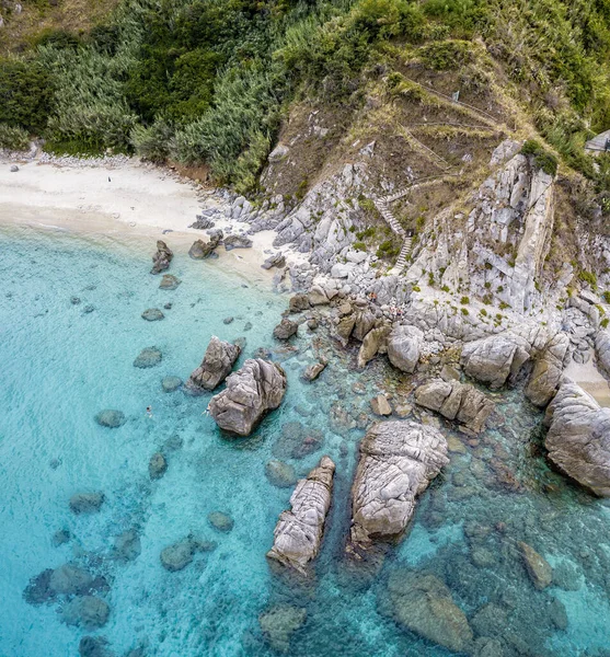 Aerial view of a beach and umbrellas. Tropea, Calabria, Italy. Parghelia. Overview of seabed seen from above, transparent water. Swimmers, bathers floating on the water. Beach and rocks of Vardanello — Stock Image Aerial View Beach Umbrellas Tropea Calabria Italy Parghelia Overview Seabed Royalty Free Stock Photos