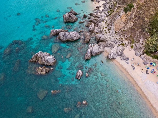 Aerial view of a beach and umbrellas. Tropea, Calabria, Italy. Parghelia. Overview of seabed seen from above, transparent water. Swimmers, bathers floating on the water. Beach and rocks of Vardanello — Stock Image Aerial View Beach Umbrellas Tropea Calabria Italy Parghelia Overview Seabed Royalty Free Stock Photos