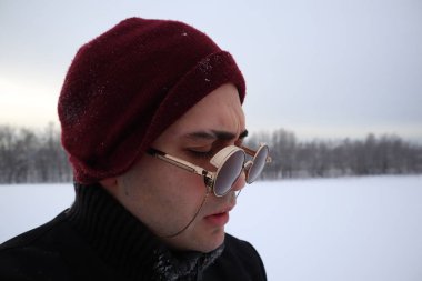 güneş gözlüğü yakışıklı genç bir alanda kışın duruyor. bir tepe üzerinde duruyor ve mesafe içine görünüyor. arka planda görkemli gökyüzü