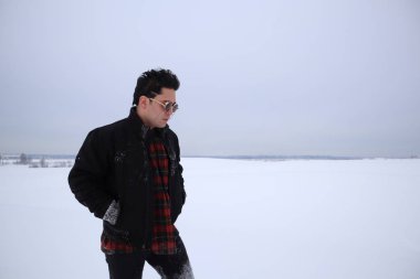 güneş gözlüğü yakışıklı genç bir alanda kışın duruyor. bir tepe üzerinde duruyor ve mesafe içine görünüyor. arka planda görkemli gökyüzü