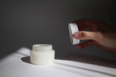 erkek el gölgeler ile beyaz arka plan üzerinde yuvarlak kapak ile Beyaz plastik tüp açılır. Tasarımınız için ön görünüm. yüz kozmetik ürünleri. Spa konsepti. Güzellik blogger, salon tedavileri kavramı. 