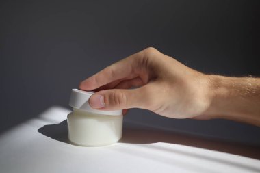 erkek el gölgeler ile beyaz arka plan üzerinde yuvarlak kapak ile Beyaz plastik tüp açılır. Tasarımınız için ön görünüm. yüz kozmetik ürünleri. Spa konsepti. Güzellik blogger, salon tedavileri kavramı. 