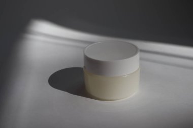 Beyaz arka planda gölgeli yuvarlak kapaklı beyaz plastik bir tüp. Tasarımın için ön görünüm. Yüz estetiği ürünleri. Spa konsepti. Güzellik blogcusu, kuaför tedavisi konsepti. 