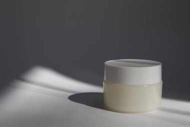 Beyaz arka planda gölgeli yuvarlak kapaklı beyaz plastik bir tüp. Tasarımın için ön görünüm. Yüz estetiği ürünleri. Spa konsepti. Güzellik blogcusu, kuaför tedavisi konsepti. 