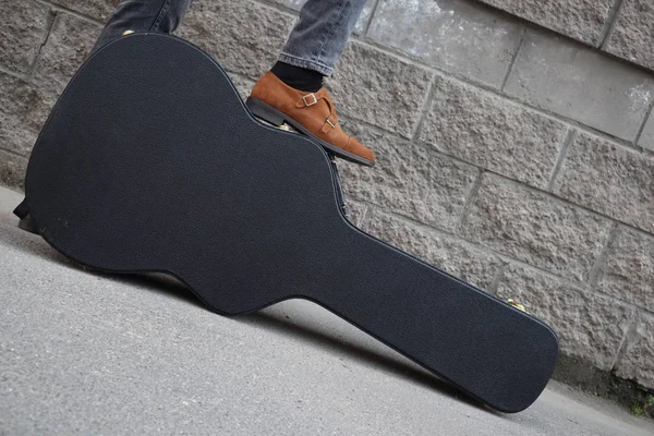男は硬いギターケースに足を置いた エレキギター用ハードケース 壁にギターケースを持ったジーンズを着た男 ギターを持つ男 スペーステキストのコピー — ストック写真