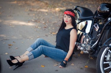 Güzel kız bisikletçi ya da sevimli kadın şık ile, uzun saçlı kot motosiklette katta oturan giyiyor.