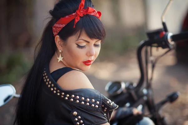 Pretty girl biker or cute woman with stylish, long hair wearing jeans sitting on floor at motorcycle. — Stock Photo, Image