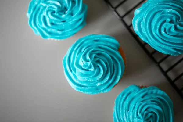 Cupcakes with blue icing on a neutral grey worktop with wire rac — Stock Photo, Image