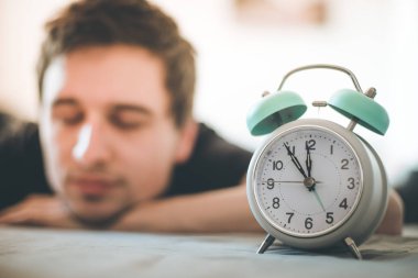 Beyaz çalar saat sabah. Genç adam arka planda uyur.