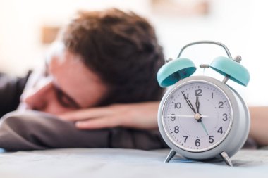 Beyaz çalar saat sabah. Genç adam arka planda uyur.