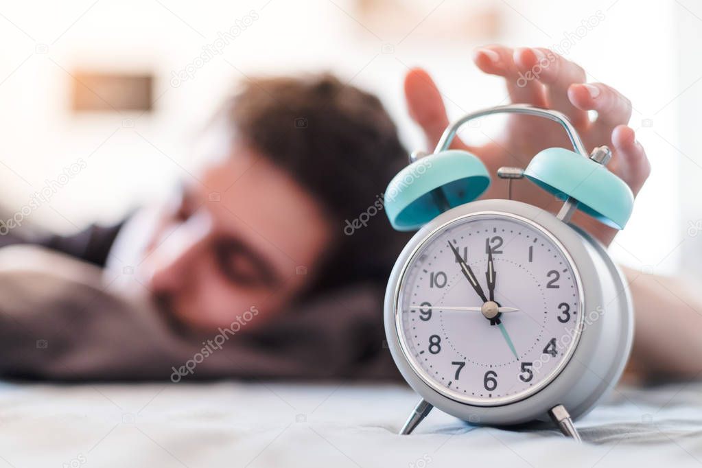 White alarm clock in the morning. Young man wakes up.