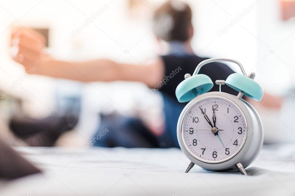 White alarm clock in the morning. Young man wakes up and stretches in the background.