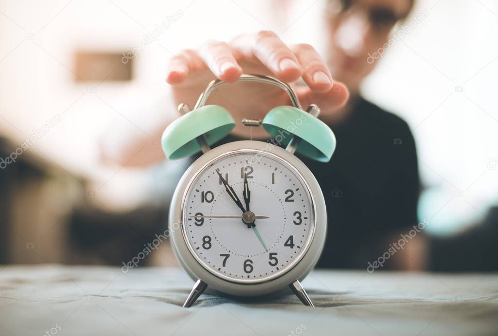 Man is pushing an alarm clock, sunshine in the morning, blurry background