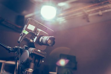 Televizyon yayın stüdyosundaki bir tripodun üzerindeki kamera, spot ışıkları ve ekipman.