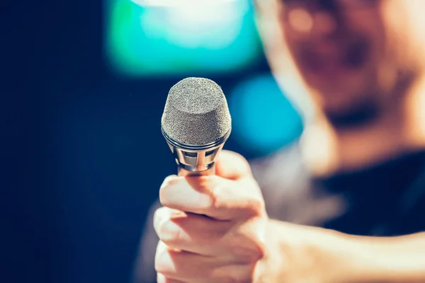 Young man on the stage is talking into a microphone, speech, face is blurry