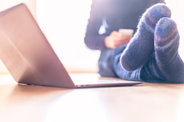 Sıcak çorap genç adam ahşap katta oturan ve gün, dizüstü ön planda sahiptir 