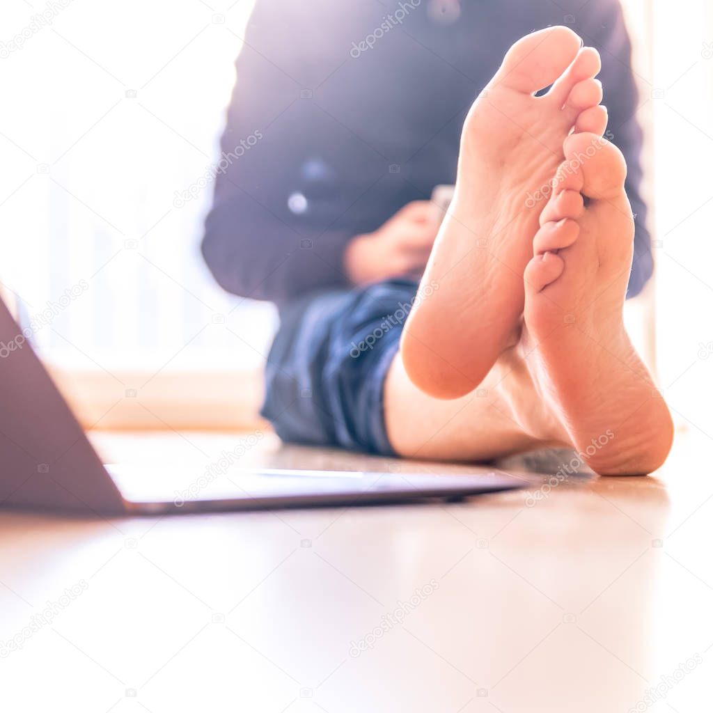 Barenaked young man is sitting on the wooden floor and enjoys the day, laptop in the foreground 