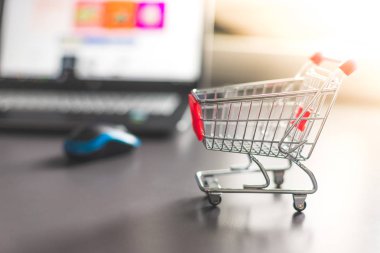 Online alışveriş kavramı: minyatür alışveriş sepeti, dizüstü bilgisayar ve fare bulanık arka planda