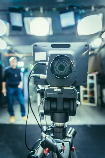 Lens of a film camera in an television broadcasting studio, spotlights and equipment, director in the background