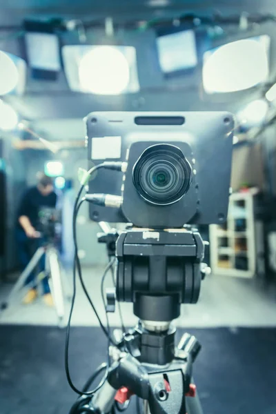 Lens of a film camera in an television broadcasting studio, spotlights and equipment, cameraman in the blurry background