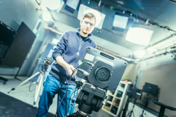 Lens of a film camera in an television broadcasting studio, spotlights and equipment, cameraman in the blurry background