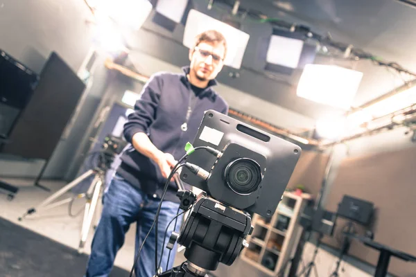 Lens of a film camera in an television broadcasting studio, spotlights and equipment, cameraman in the blurry background
