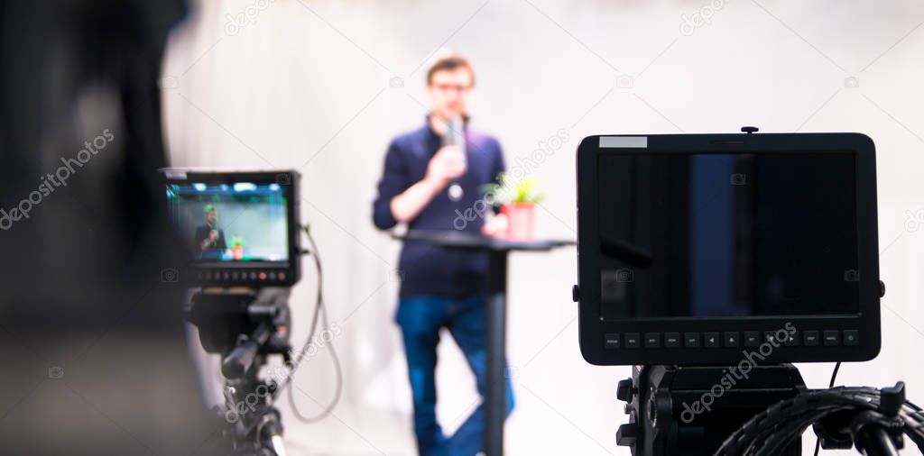 Male journalist in a television studio talks into a microphone, film cameras