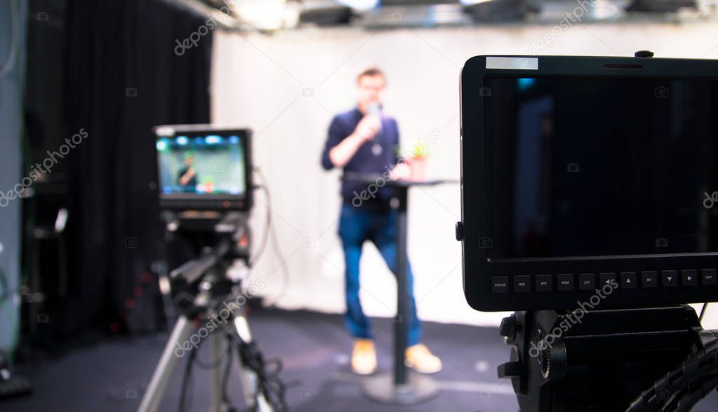 Male journalist in a television studio talks into a microphone, film cameras