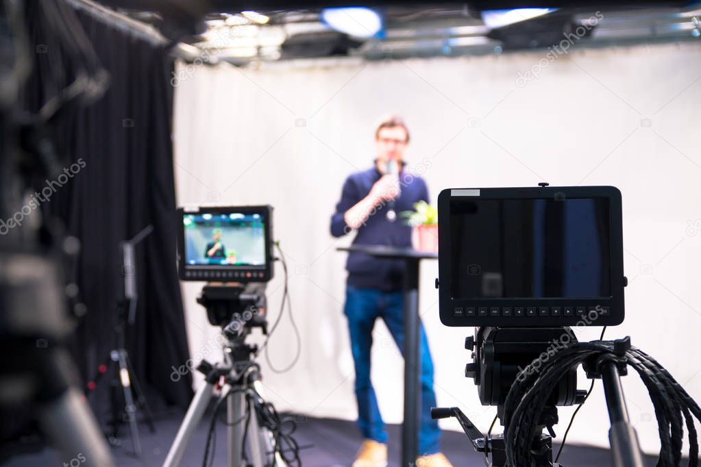 Male journalist in a television studio talks into a microphone, film cameras