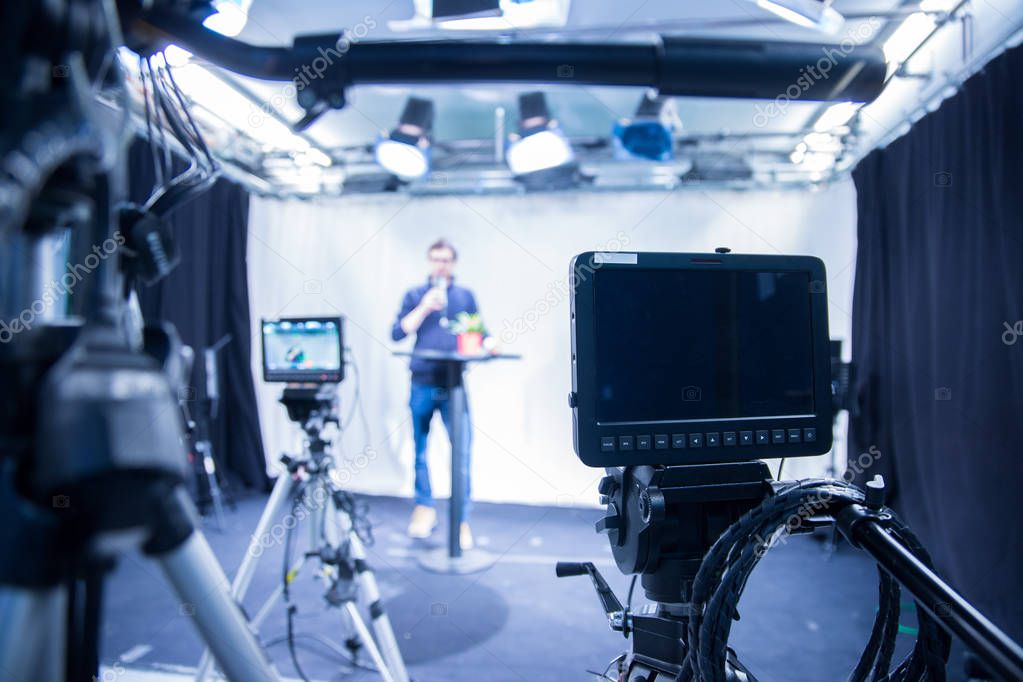 Male journalist in a television studio talks into a microphone, film cameras