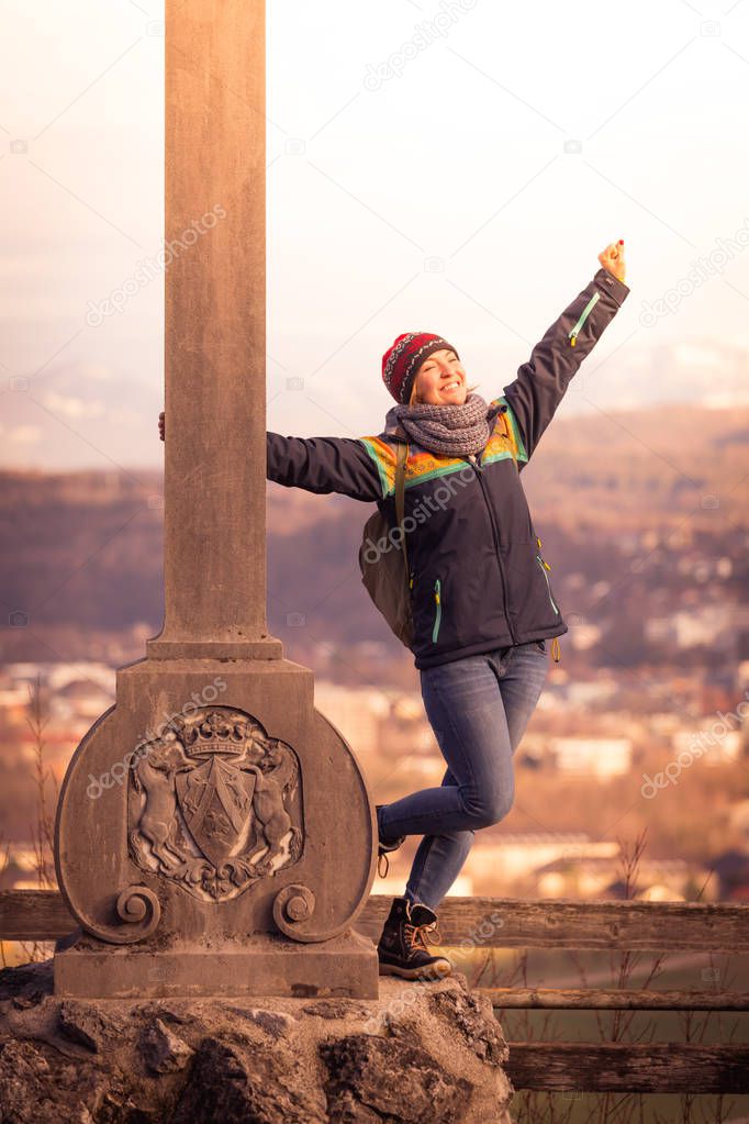 Young girl stands proud and happy on a summit cross, autumn