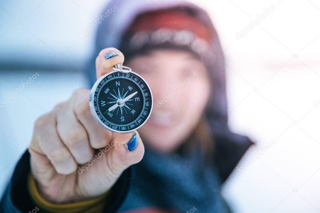 Young smiling woman holds up a compass. Wintertime, gloves and hood.