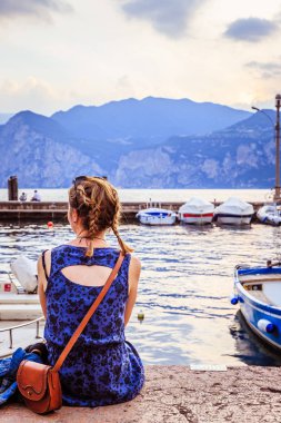 Mavi elbise genç güzel kızla Malcesine kıyı sahil üzerinde oturan ve görünüme sahiptir. Lago di Garda.