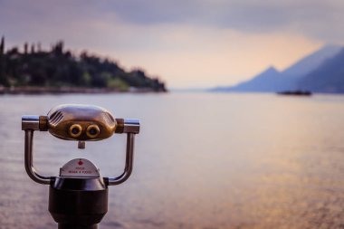 Tourist binoculars on the lake Lago di Garda, evening scene with water and mountains clipart
