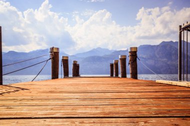 Ahşap dock iskele, mavi göl, dağlar ve gökyüzü bulutlu, lago di garda, İtalya. 