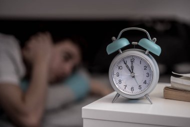 Beyaz çalar saat komidinin üzerinde. Arka planda, uykusuzluk uyku genç çalışır