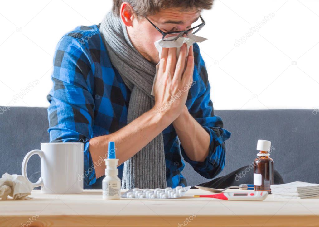 Young caucasian man in blue shirt is having a cold, sneezing in a tissue