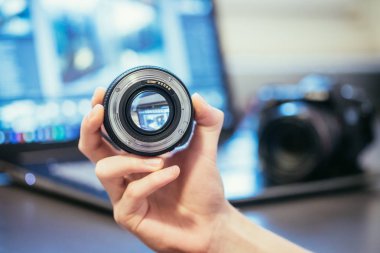 Fotoğrafçı bir profesyonel fotoğraf optik elinde tutuyor. Kamera ve dizüstü bulanık arka planda. 
