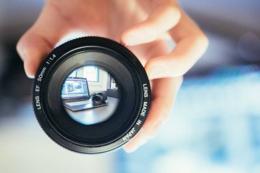 Fotoğrafçı elinde profesyonel bir fotoğraf optiği tutuyor. Bulanık arkaplanda dizüstü bilgisayar. 