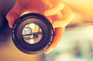 Fotoğrafçı elinde profesyonel bir fotoğraf optiği tutuyor. Bulanık arkaplanda dizüstü bilgisayar. 