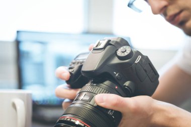 Fotoğrafçı telefoto lens ile profesyonel bir fotoğraf elinde, dizüstü bulanık arka planda tutuyor