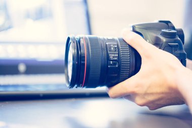Fotoğrafçı telefoto lens ile profesyonel bir fotoğraf elinde, dizüstü bulanık arka planda tutuyor