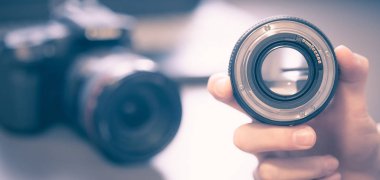Fotoğrafçı bir profesyonel fotoğraf optik elinde tutuyor. Kamera ve dizüstü bulanık arka planda.