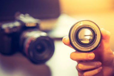 Fotoğrafçı bir profesyonel fotoğraf optik elinde tutuyor. Kamera ve dizüstü bulanık arka planda.