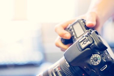 Fotoğrafçı telefoto lens ile profesyonel bir fotoğraf elinde, dizüstü bulanık arka planda tutuyor