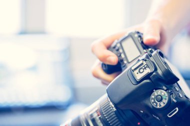 Fotoğrafçı bir refleks kamera telefoto lens ile elinde tutuyor. Tablo ve bulanık arka plan içinde laptop