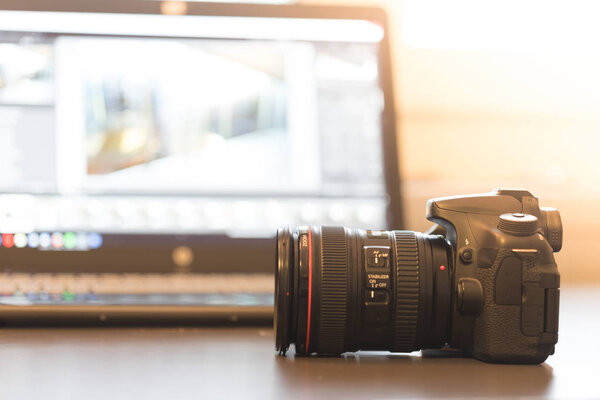 Professional camera with telephoto lens on a table, laptop in the blurry background