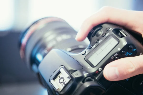 Photographer is holding a professional camera with telephoto lens in his hand, laptop in the blurry background